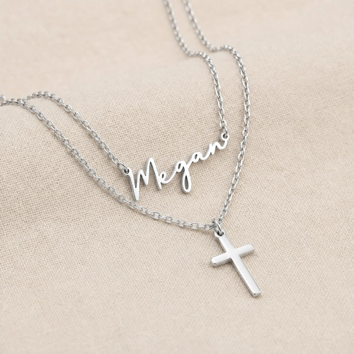 Silver personalised name and cross layered necklace set on neutral linen - Dahlia font